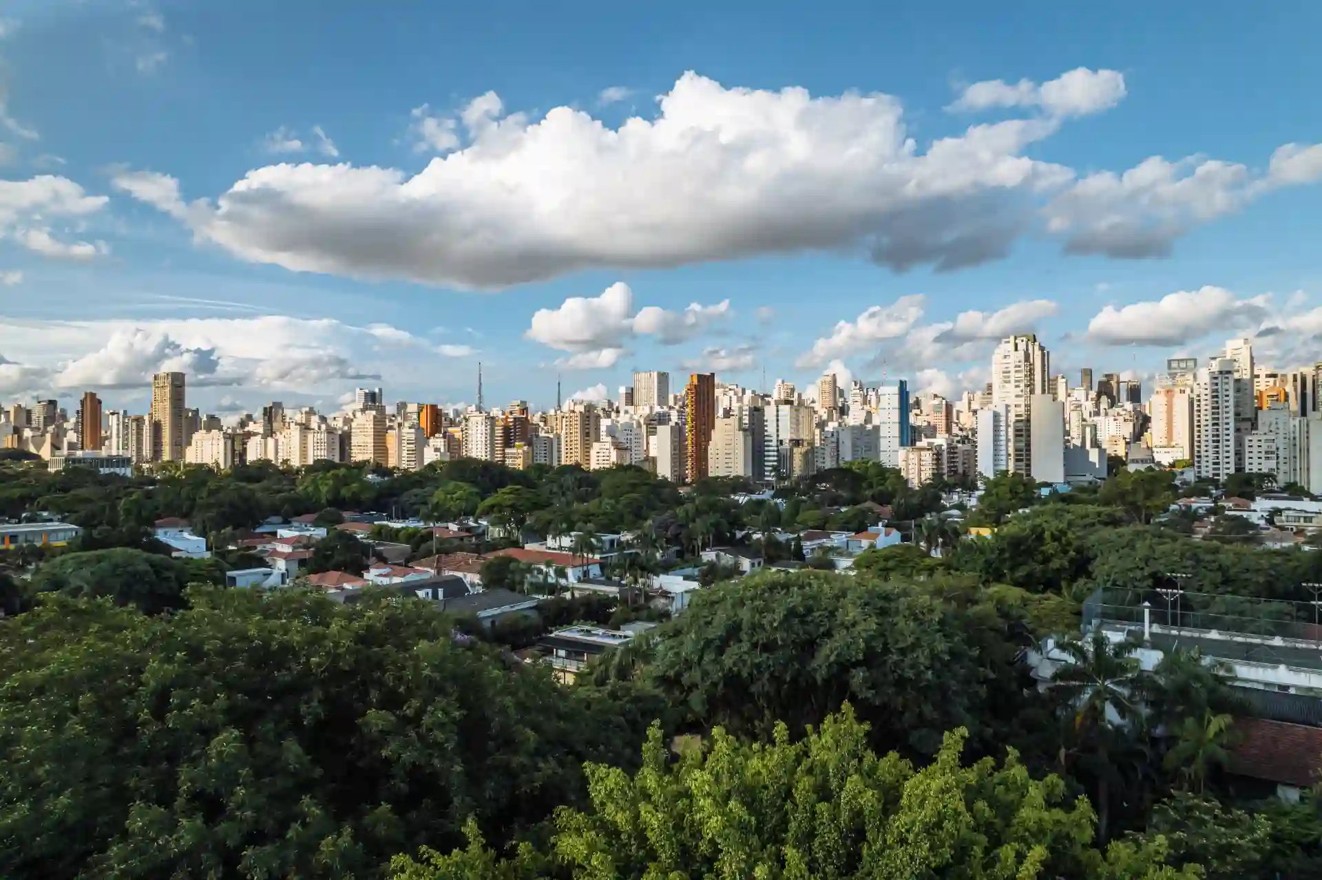Vista panorâmica de uma cidade moderna com arranha-céus e muito verde, sob céu com nuvens brancas. Ideal para quem busca imagens de cidades grandes e arquitetura urbana.