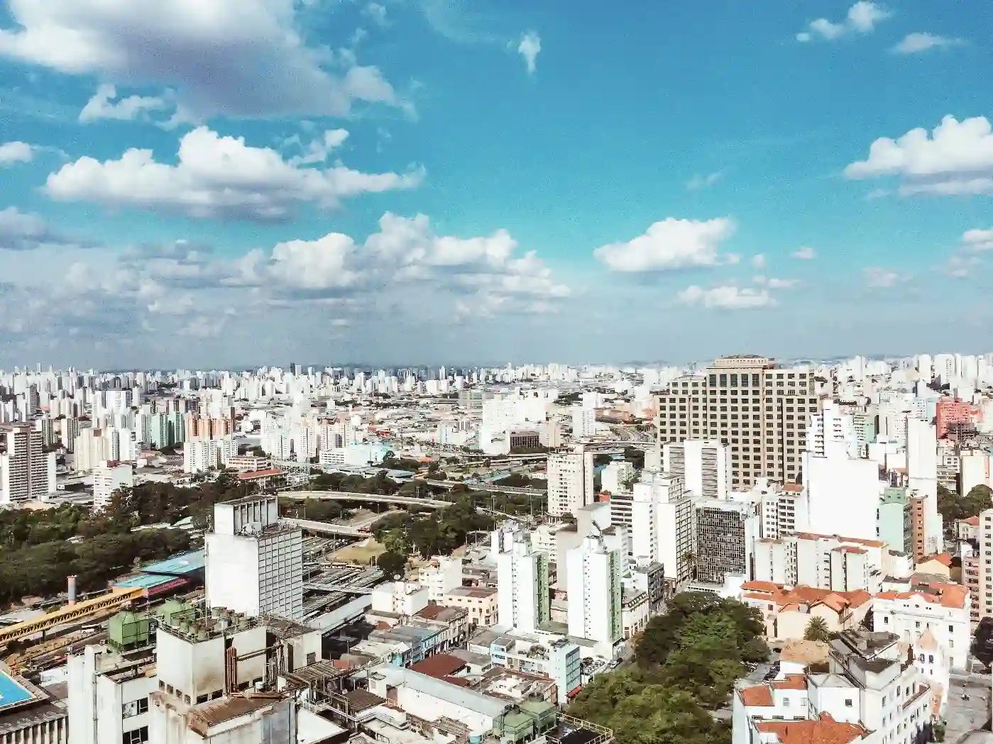 Vista aérea de uma cidade com muitos prédios altos sob céu parcialmente nublado, destacando-se pelo ambiente urbano e moderno