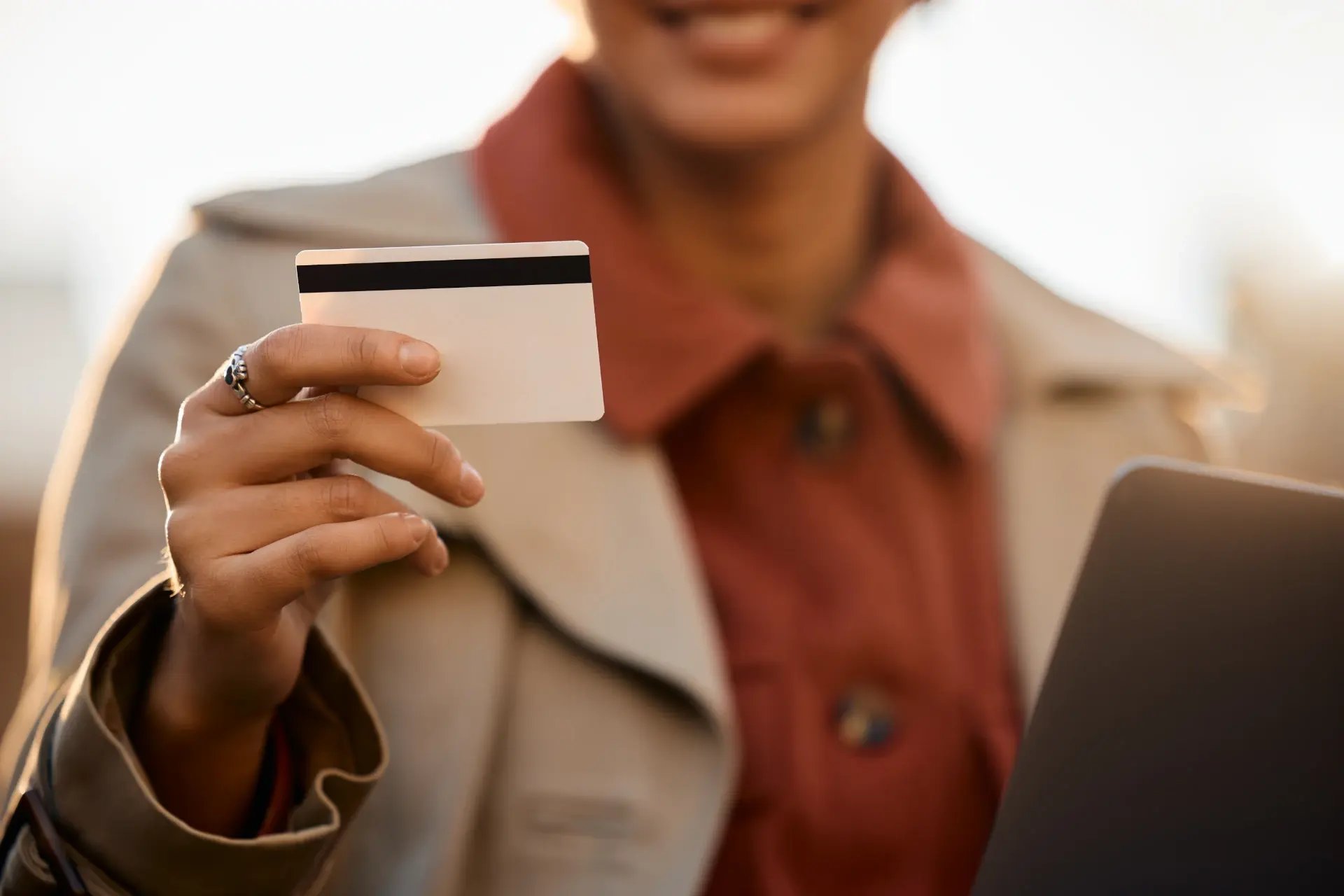 Pessoa segurando um cartão de crédito e usando um laptop, representando compras e transações financeiras online de forma segura.