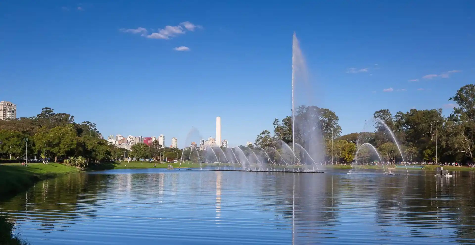 Imagem do Parque Ibirapuera em São Paulo com fonte de água e natureza, cenário urbano ao fundo e céu azul claro, ideal para lazer e descanso na cidade.