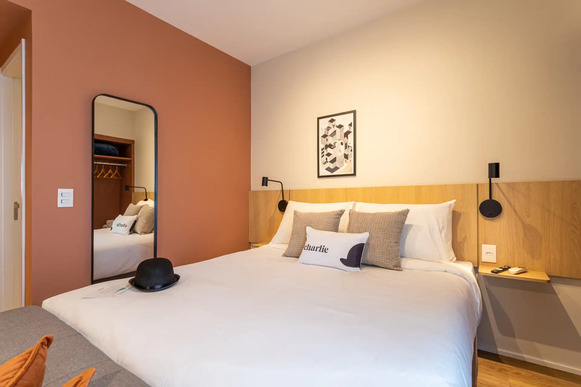 Quarto de hotel moderno com cama confortável, decoração minimalista, espelho grande, quadros nas paredes, iluminação aconchegante, ideal para descanso e viagens.